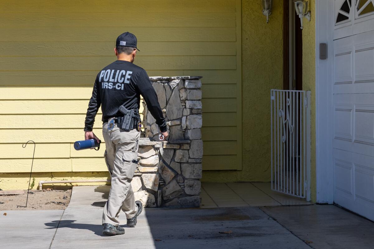 A person wearing a shirt that says "Police" walks toward a house.