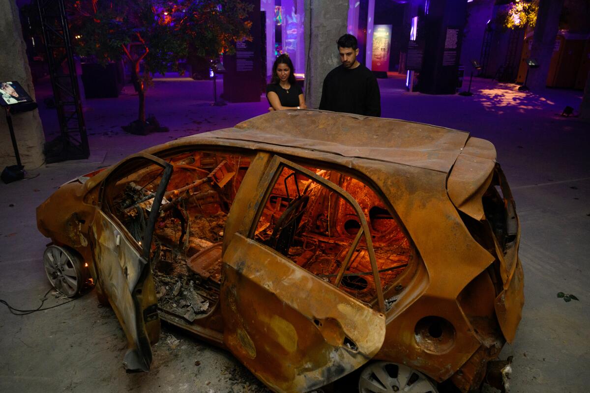 Two people look at a destroyed car at an exhibition.