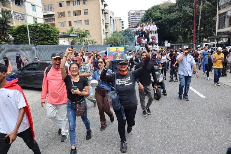 Protesters raise a fist in solidarity and hold up pictures of Edmundo Gonzalez as they walk down the street in Caracas.