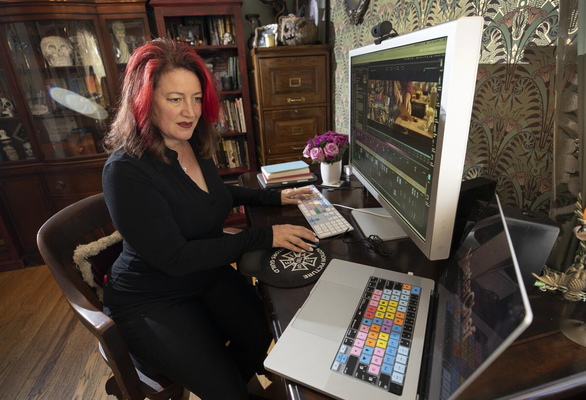 A woman working at a computer and a monitor at a desk in a room with bookcases.