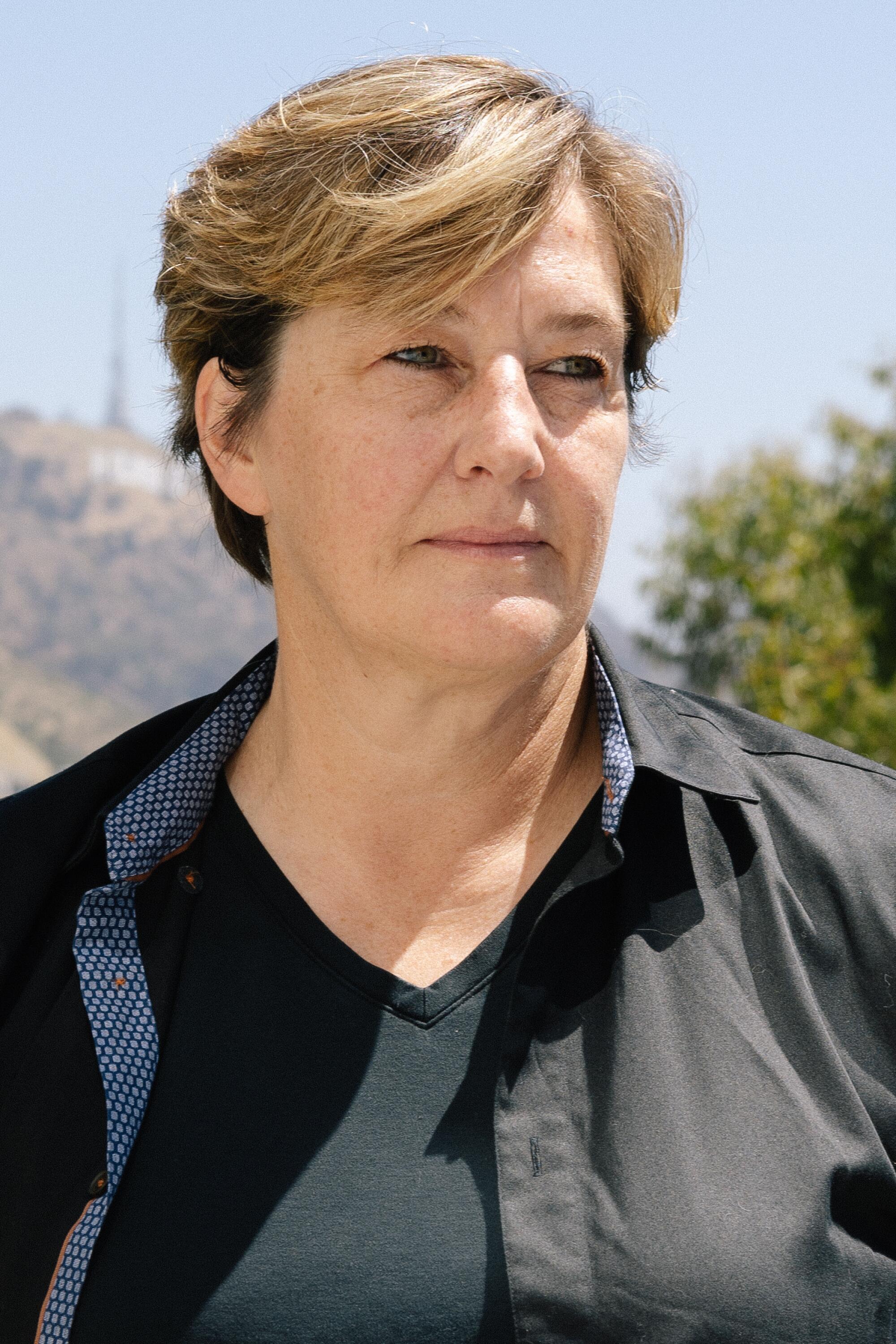 A woman with short blond hair in a dark shirt. The Hollywood hills are seen behind her.