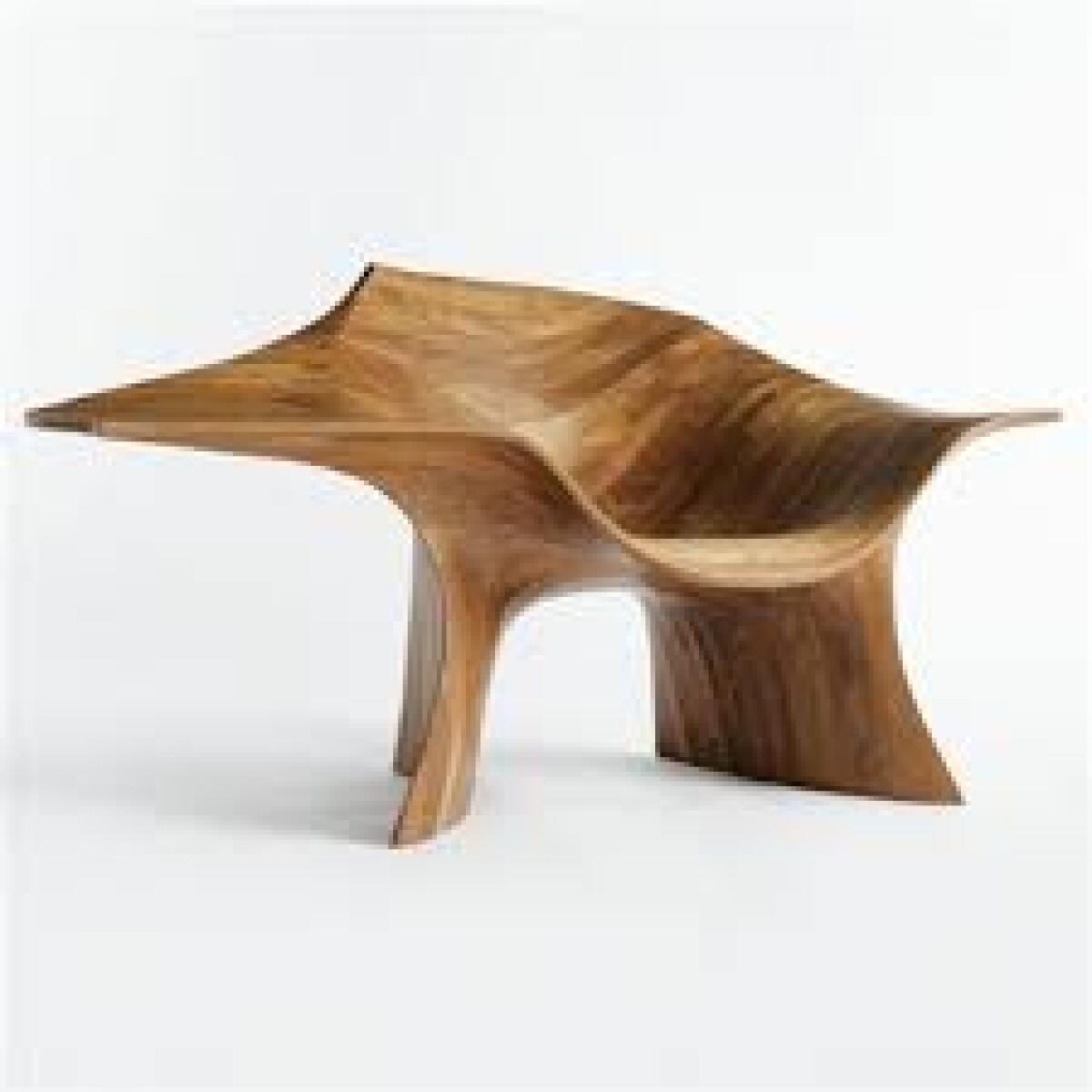 An asymmetrical, curvilinear chair carved from walnut looks sleek and sculptural set against a stark white background.