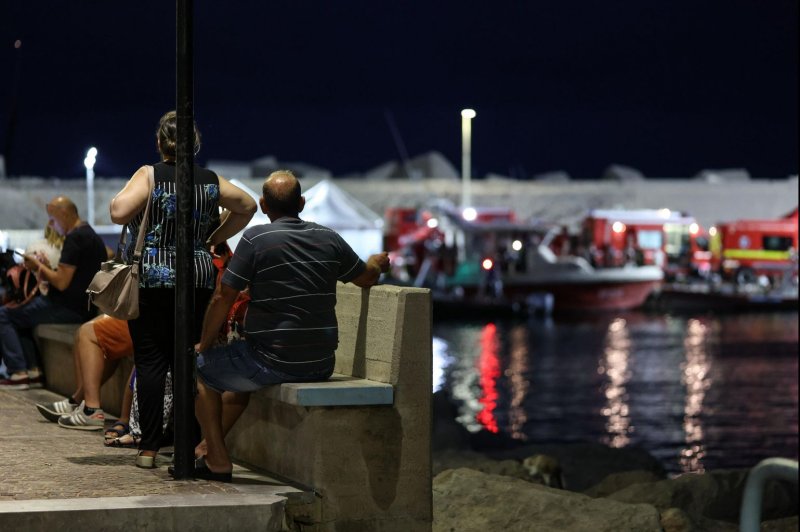 Bystanders on the quayside in Porticello, Sicily, as rescue workers and divers worked late into the night Tuesday in a race against to time to try to find six people missing from a superyacht owned by British tech-billonaire Mike Lynch that went down in a storm in the earlly hours of Monday with him and his wife, daughter and 19 other guests and crew on board. Photo by Igor Petyx/EPA-EFE