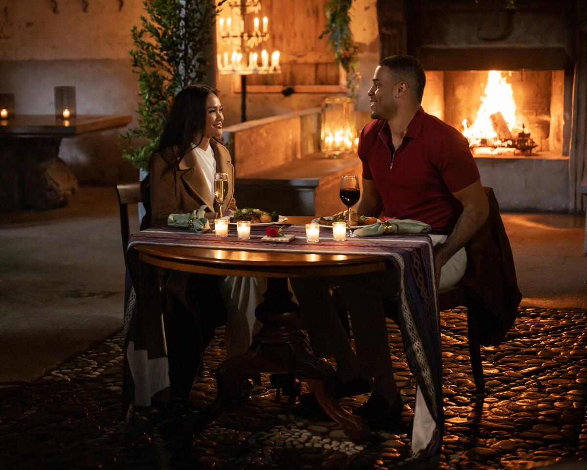 A woman and man sitting a table with a fire burning in a fireplace behind them.