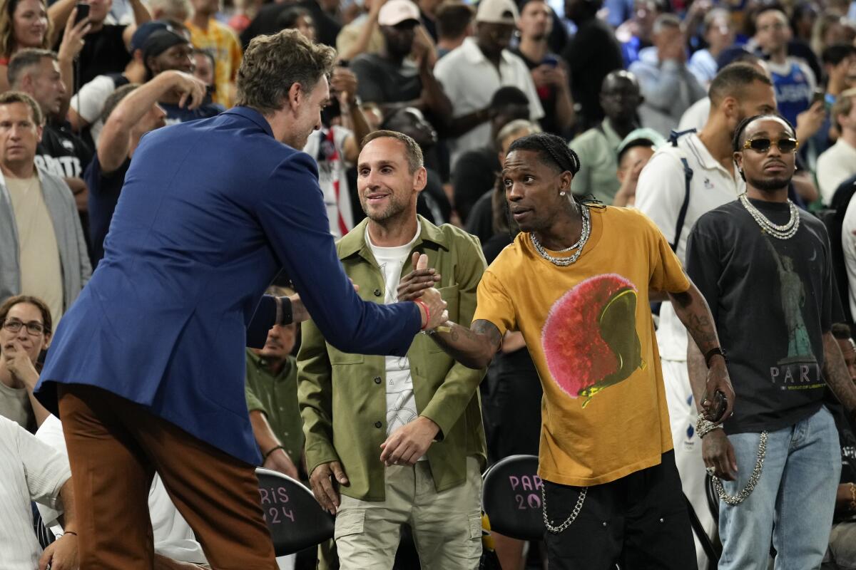 Pau Gasol in a blue suit shakes hands with rapper Travis Scott at a basketball game