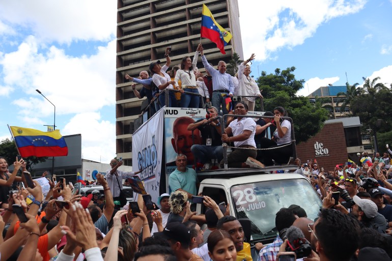 Maria Corina Machado and Edmundo Gonzalez wave a Venezuelan flag atop a truck surrounded by supporters in Caracas.