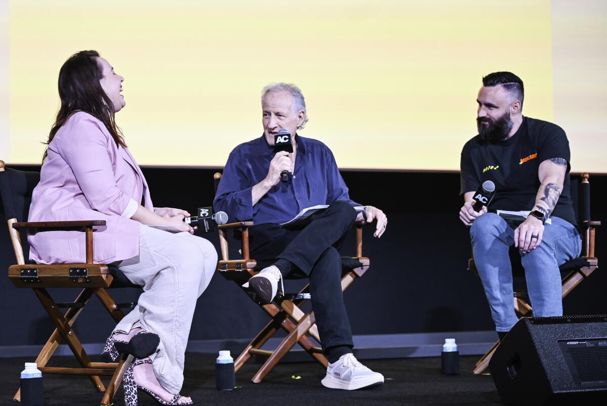 Three people discuss a movie on stage while sitting in chairs.