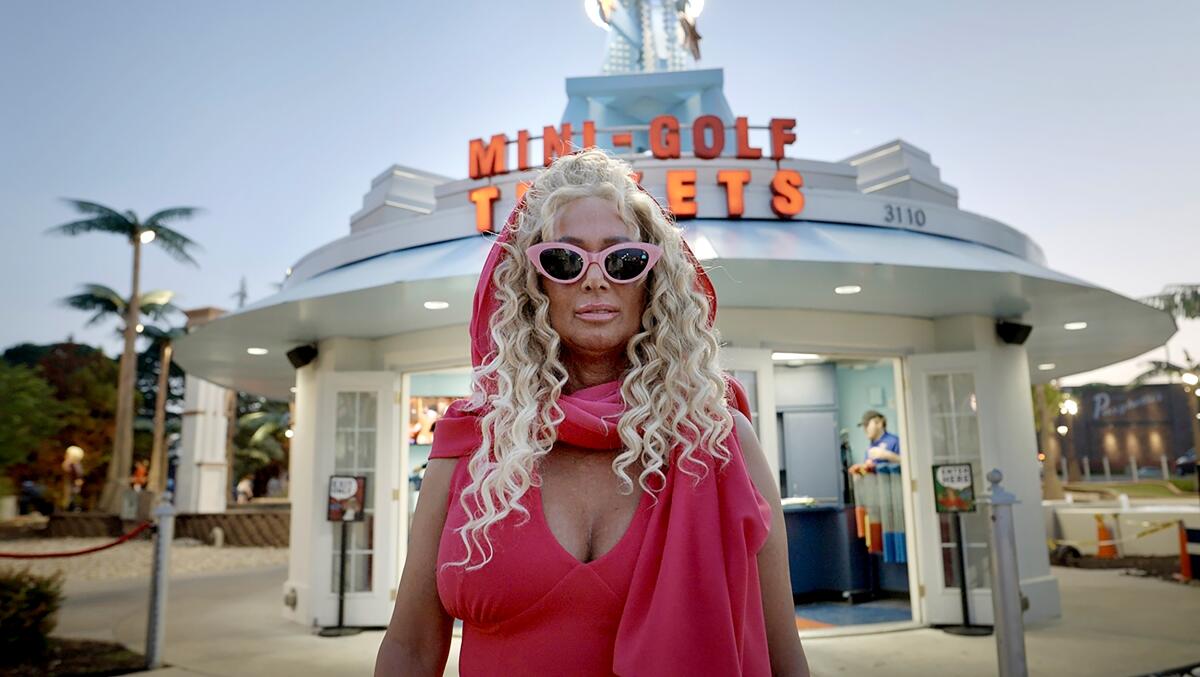 A woman in a pink outfit stands in front of a mini-golf place.