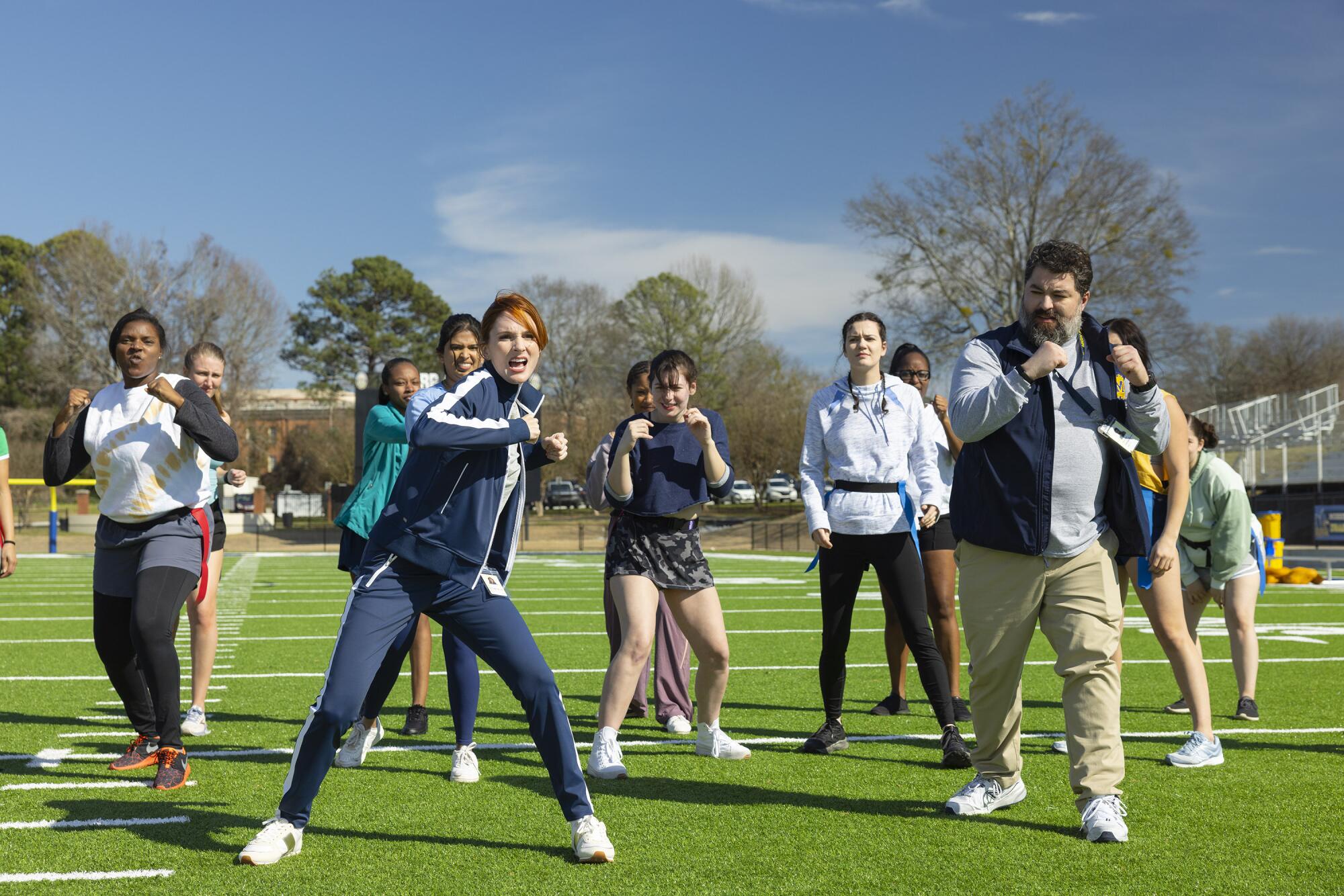 Two coaches standing in front of a group of girls with their fists in the air on a green football field.