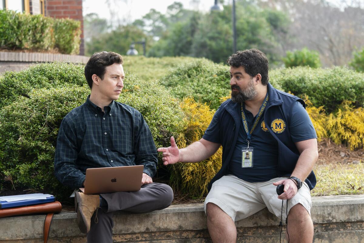 Two men seated on a retaining wall.