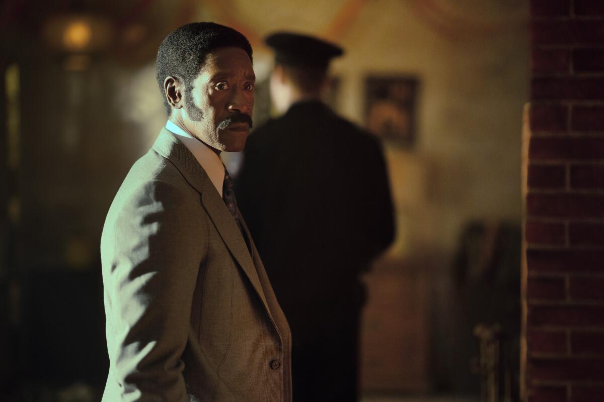 A profile shot of a man with a mustache in a tan suit.