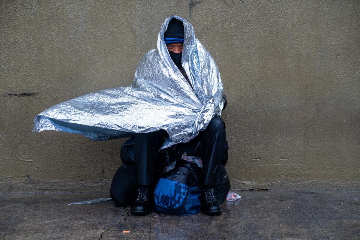 A man in a silver sheet sits on the sidewalk in Skid Row.