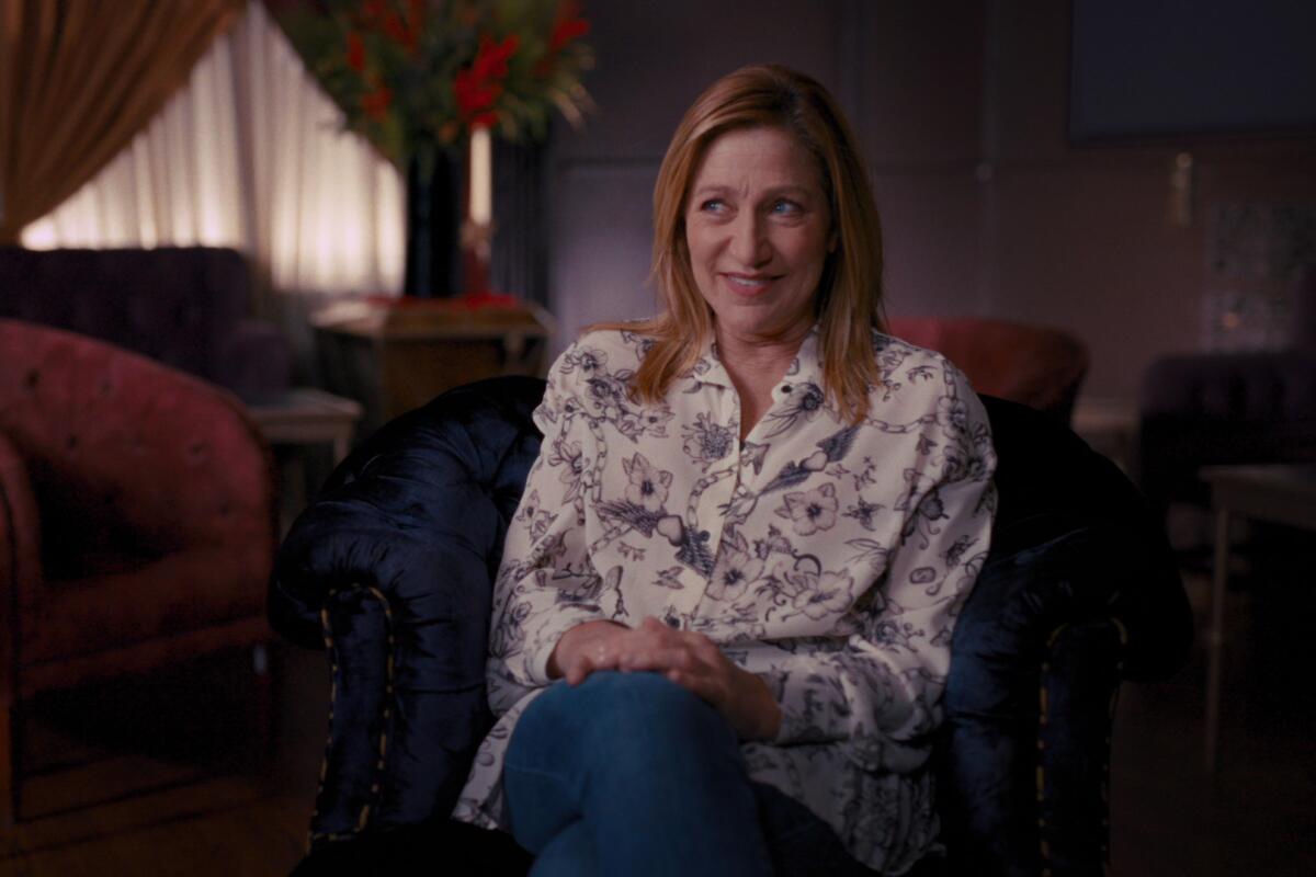 Edie Falco seated with her hands resting on her crossed legs.