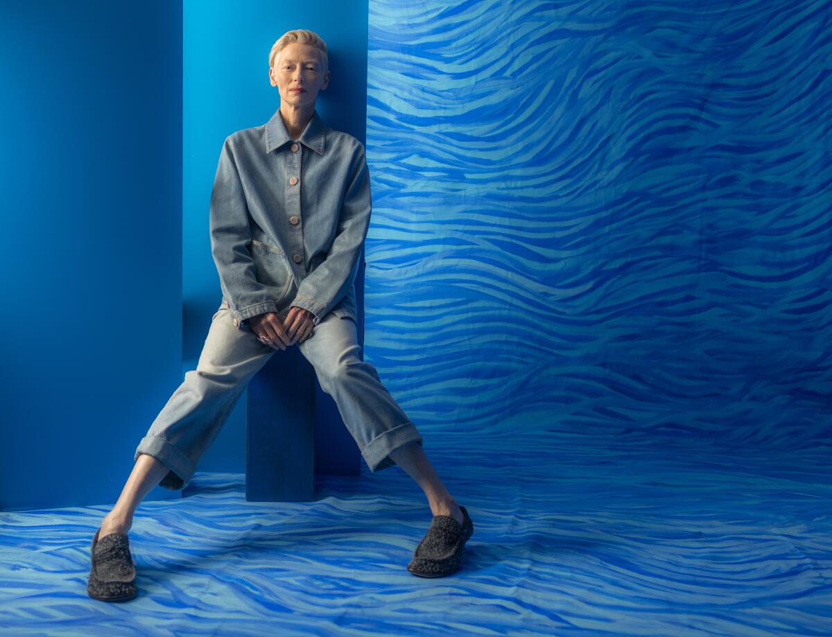 Tilda Swinton sits in a room with blue waves designs on the walls and floor