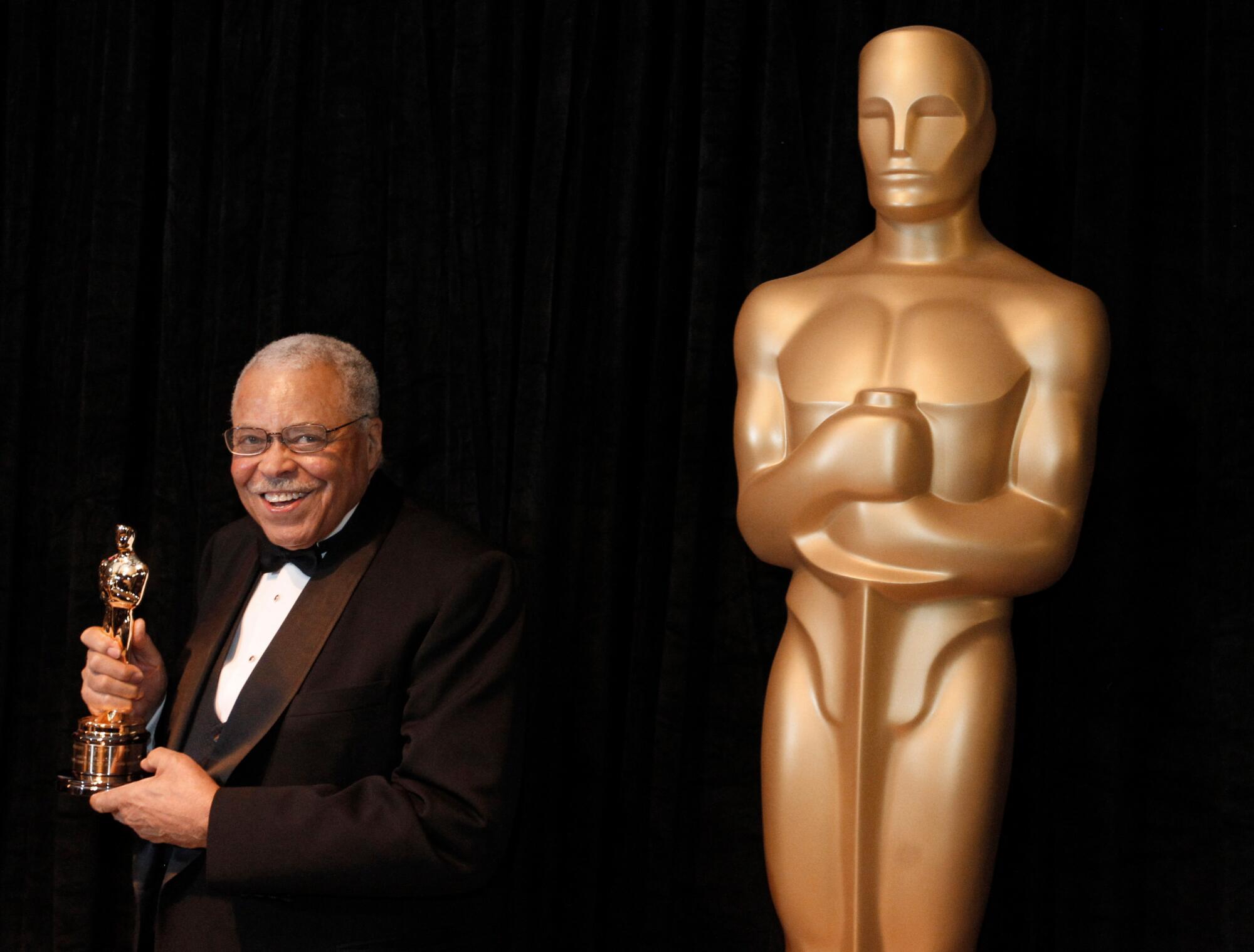 James Earl Jones holds an Oscar statuette and stands next to an oversize statue of an  Academy Award.