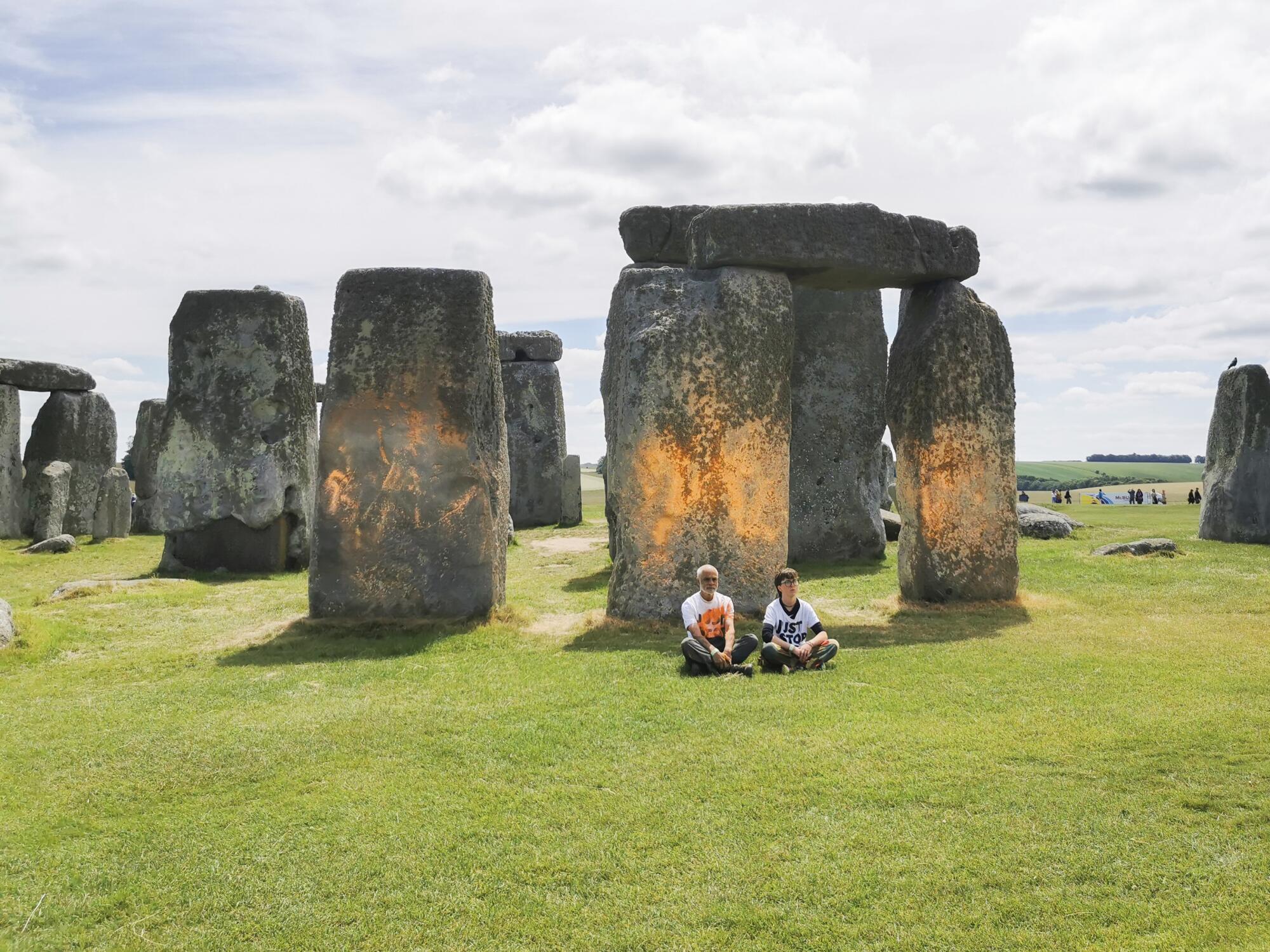 Protesters sit in front of a spray-painted Stonehenge.