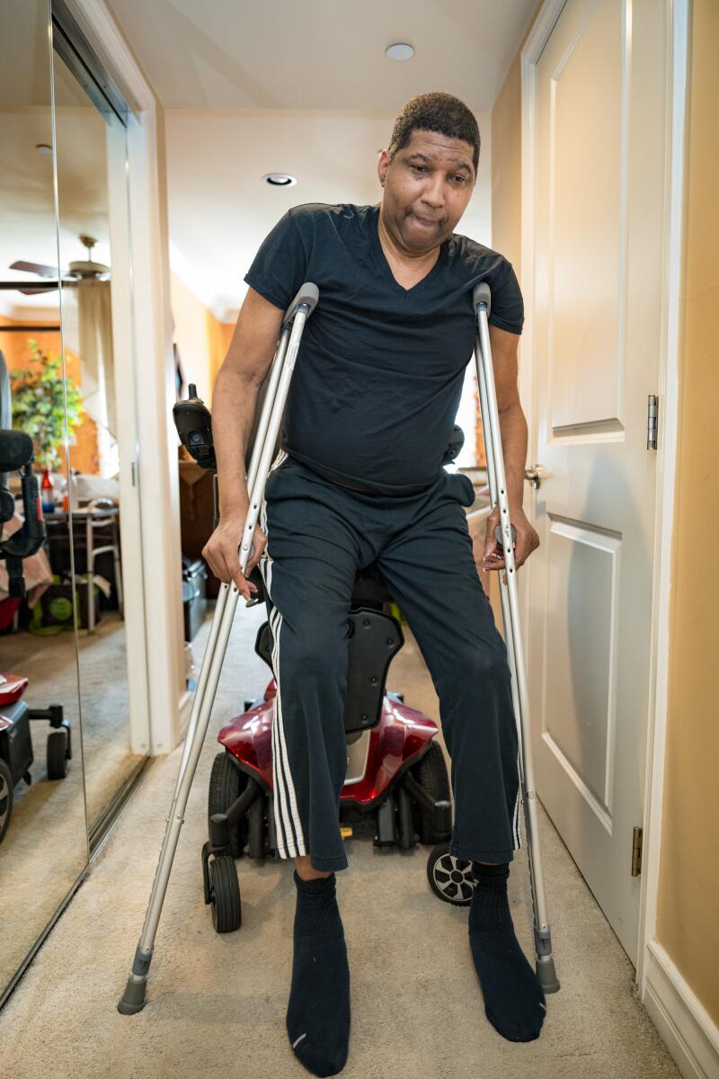 Rod Foster struggles to stand with his crutches as he moves away from his wheelchair.