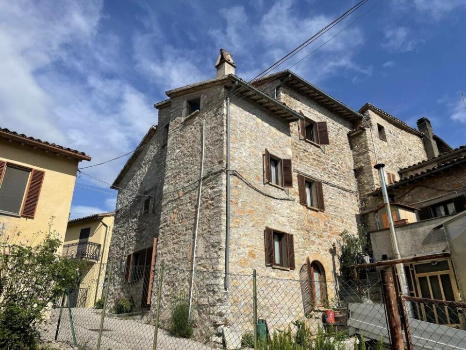 The cottage in Sellano, Italy has an exposed stone interior, a kitchen with a fireplace and a cosy living room