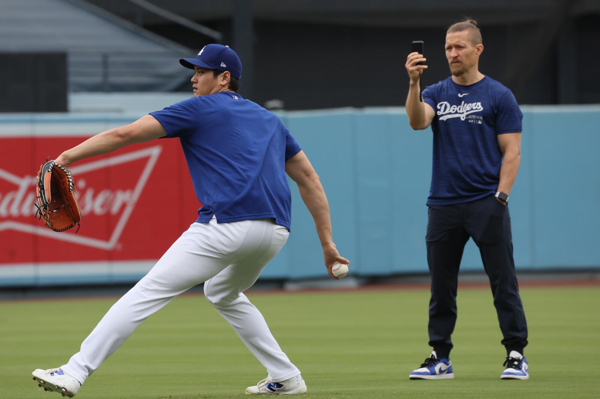 Dodgers two-way player Shohei Ohtani throws warm-up pitches under the watchful eye of athletic trainer Thomas Albert