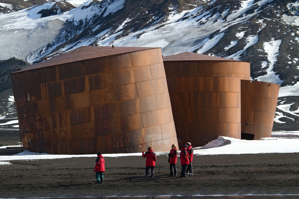 Tourists from a cruise ship explore near derelict whale oil tanks on beach