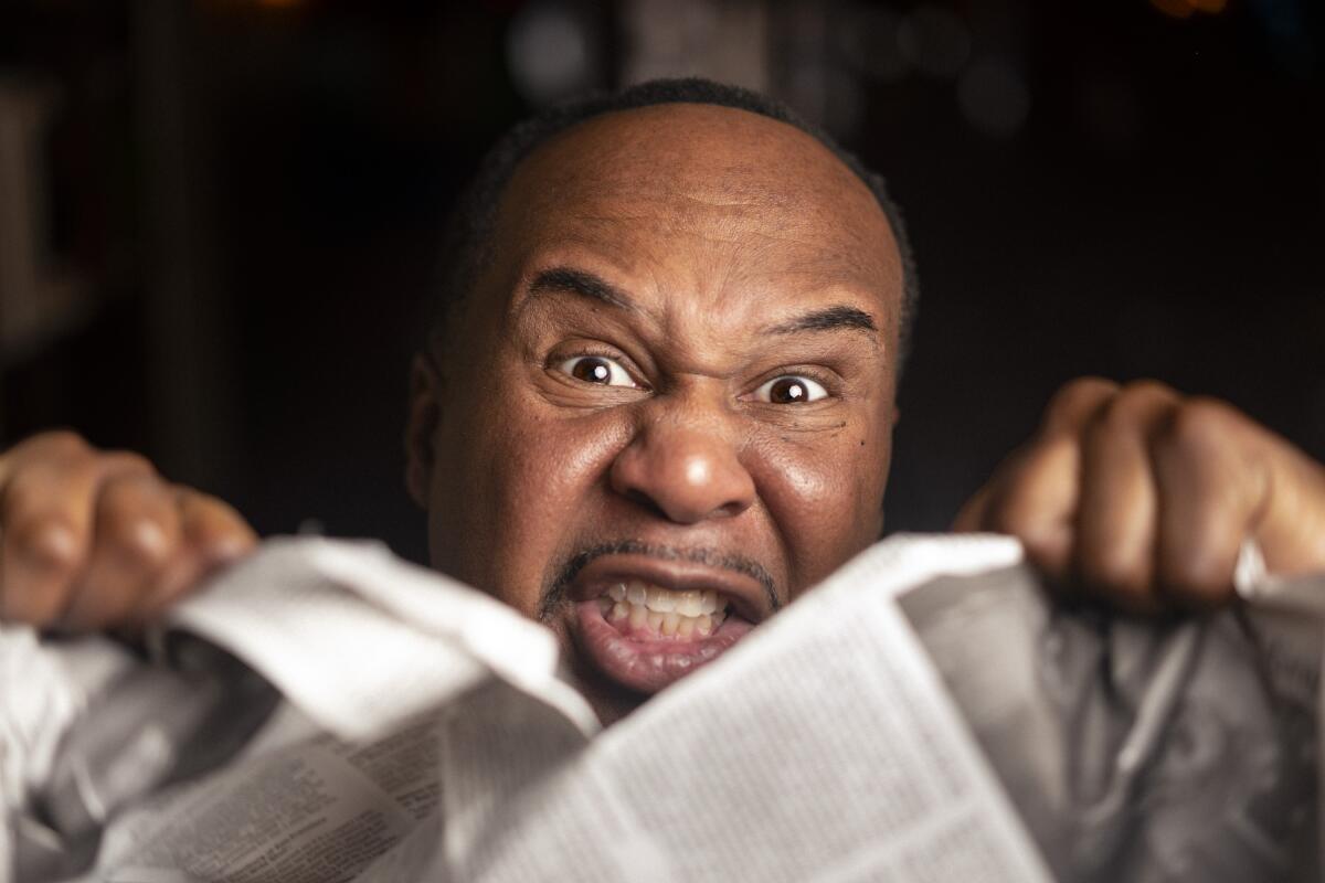 A close up of a man's face grimacing and ripping a newspaper in two.