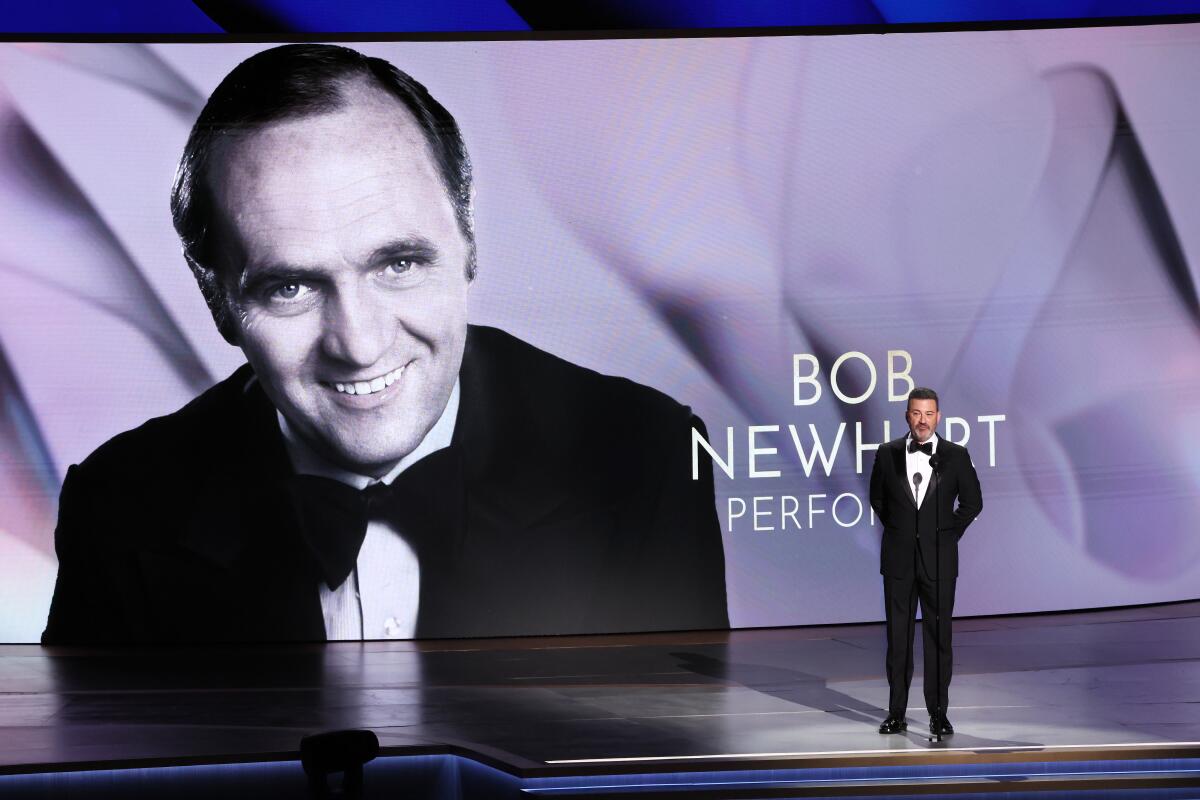 A black and white image of Bob Newhart on a screen with Jimmy Kimmel standing in front of it.