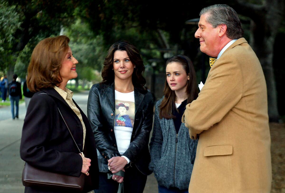 A woman and her daughter stand outdoors watching her parents smiling at each other. 