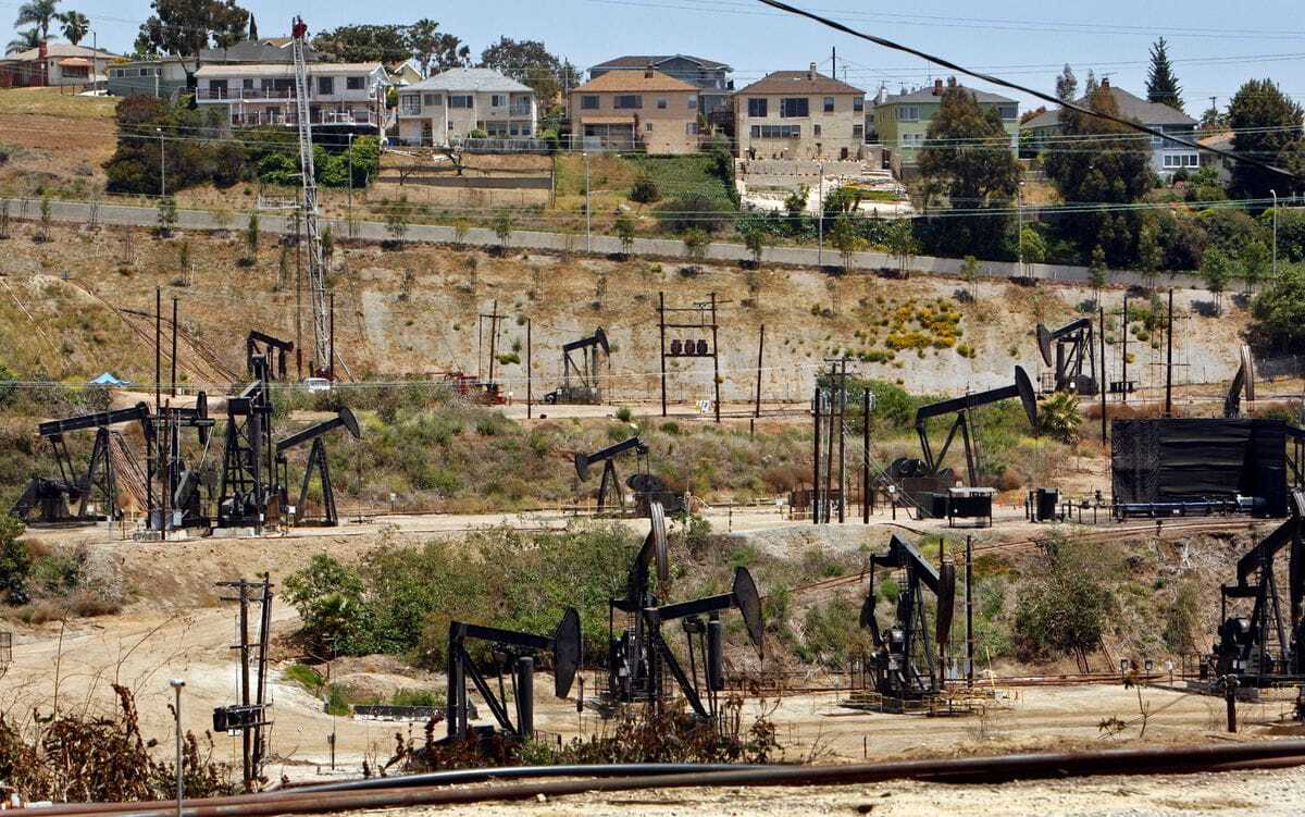 A view of pumpjacks, with homes on higher ground