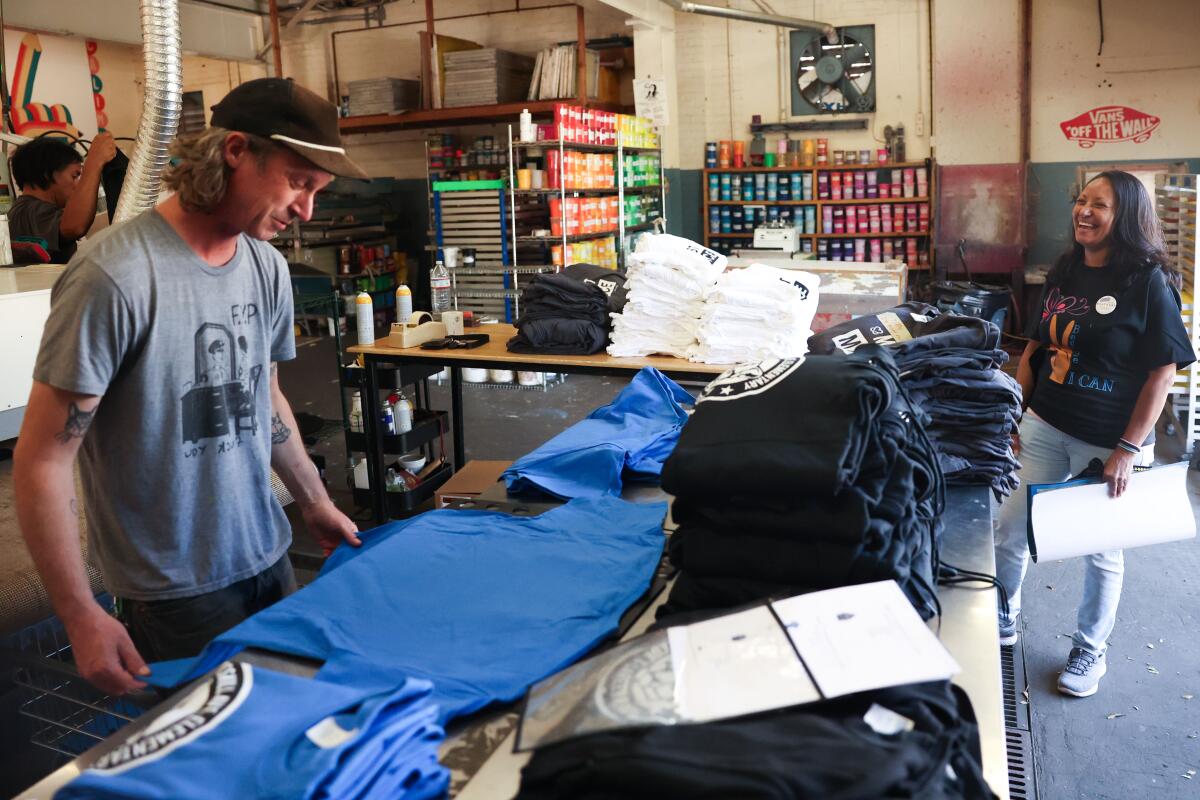 A man looks at a T-shirt on a table full of them.