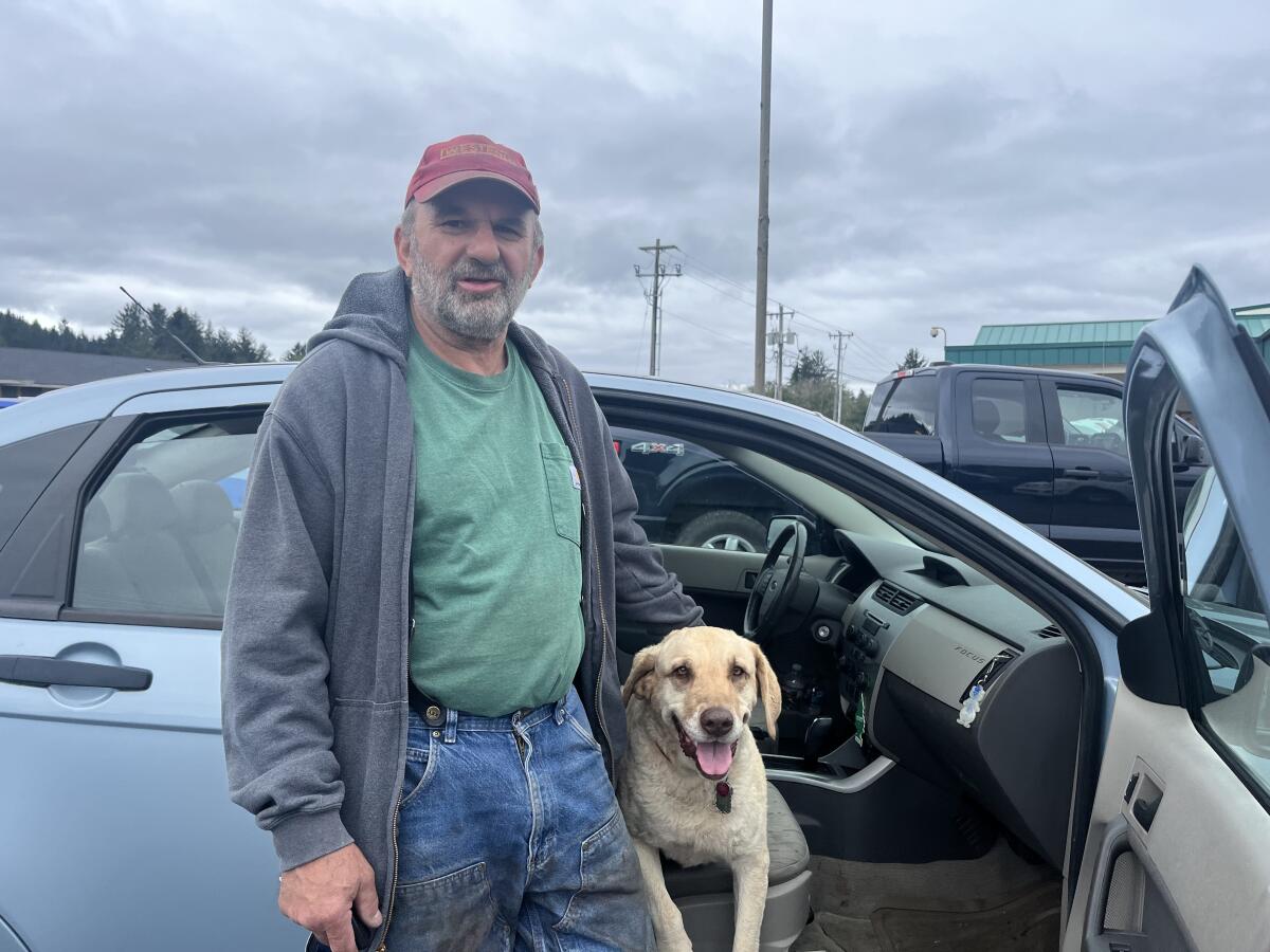 A man poses with his dog, seated on the front seat of his car