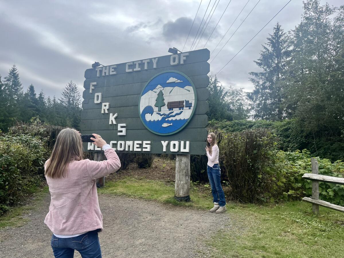 A woman takes a picture in front of a sign welcoming visitors to Forks, Wash.