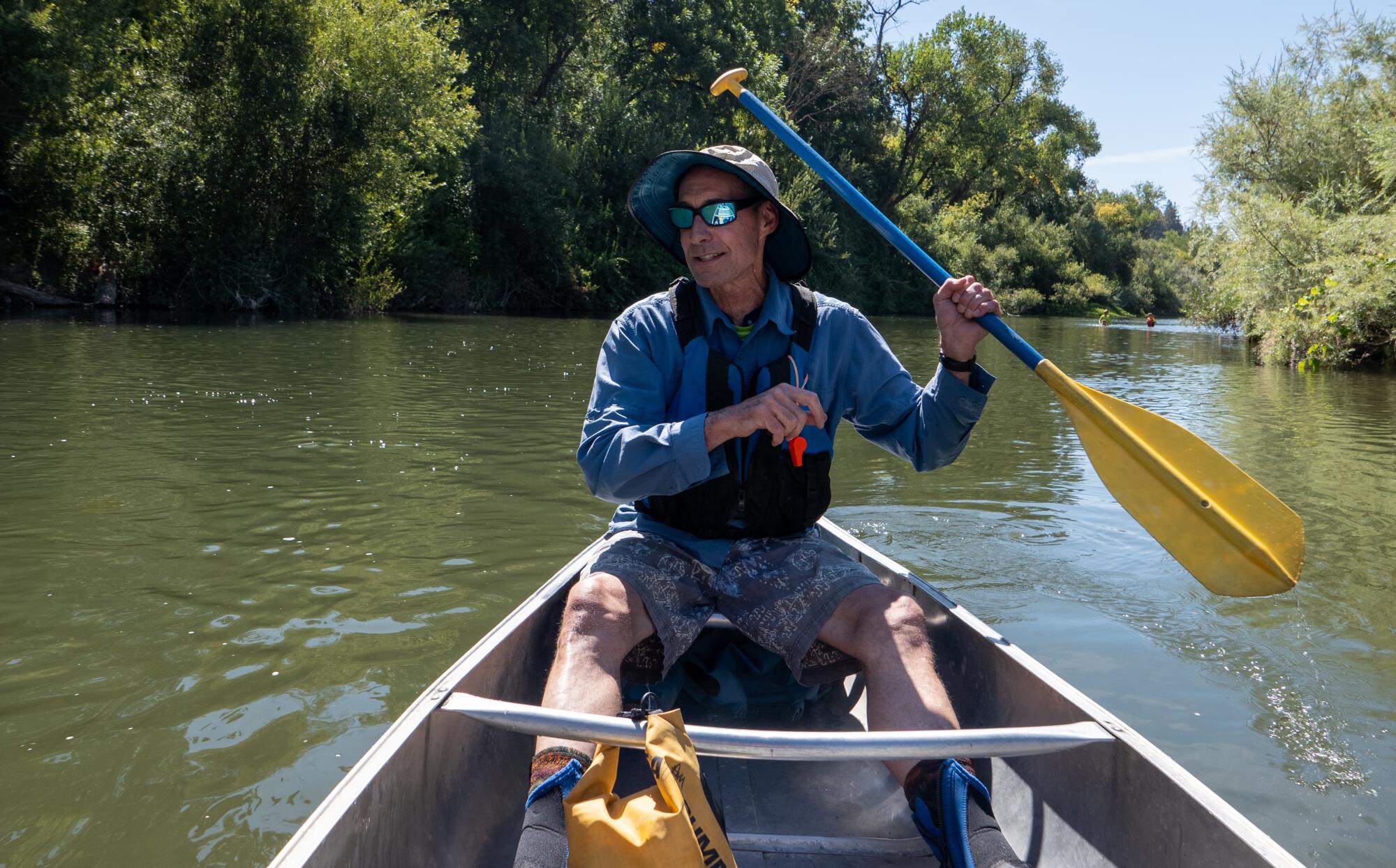 Don McEnhill, wearing sunglasses and a sunhat, paddles a canoe along the Russian River.