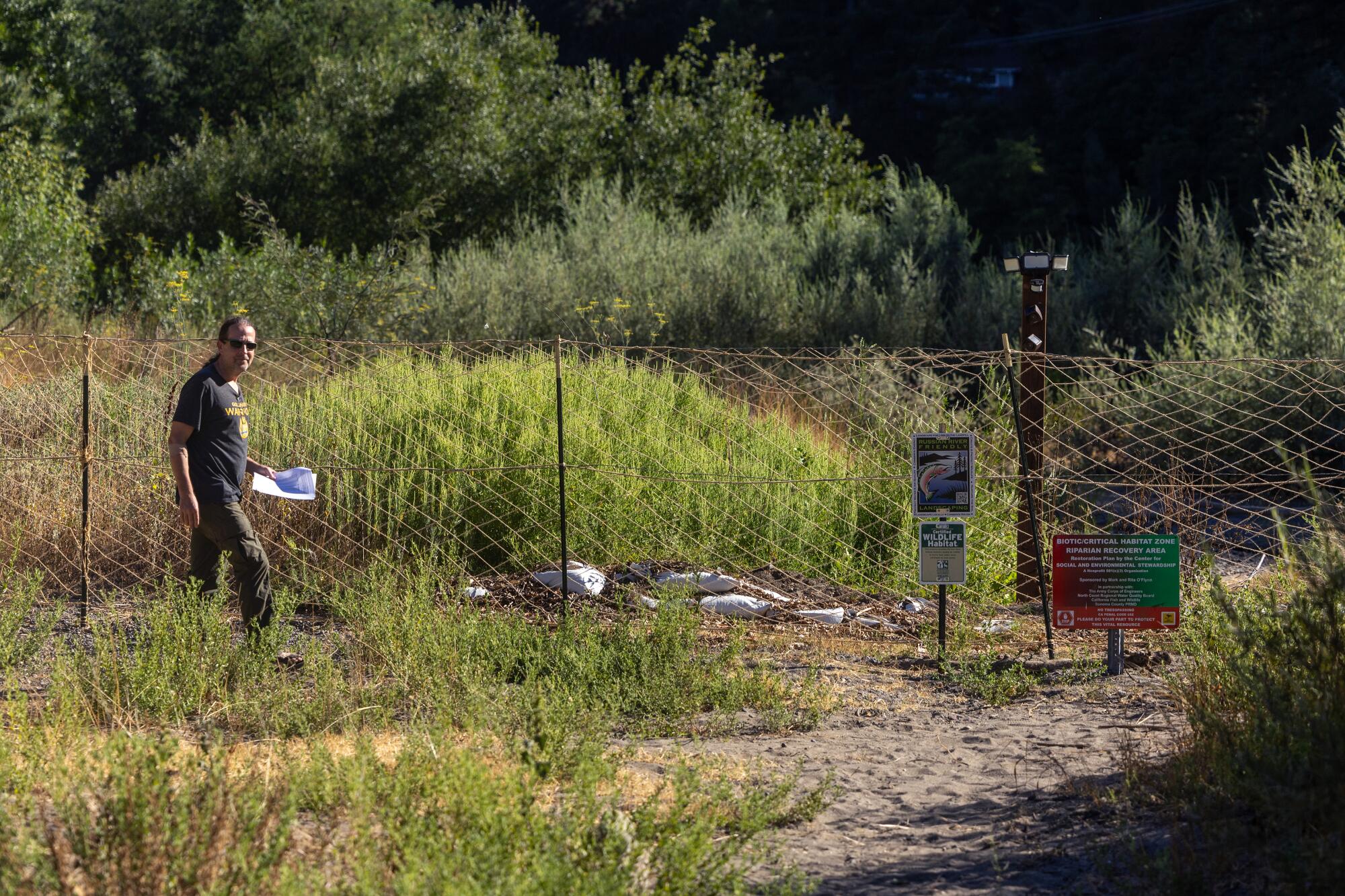 A man walks alongside a mesh fence blocking access to riverfront property.