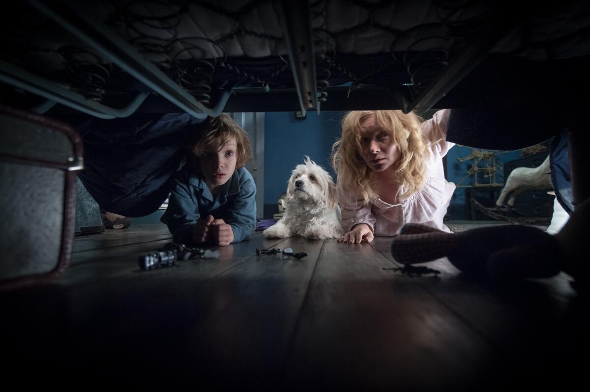 A boy, a dog and a woman look under a bed for monsters.