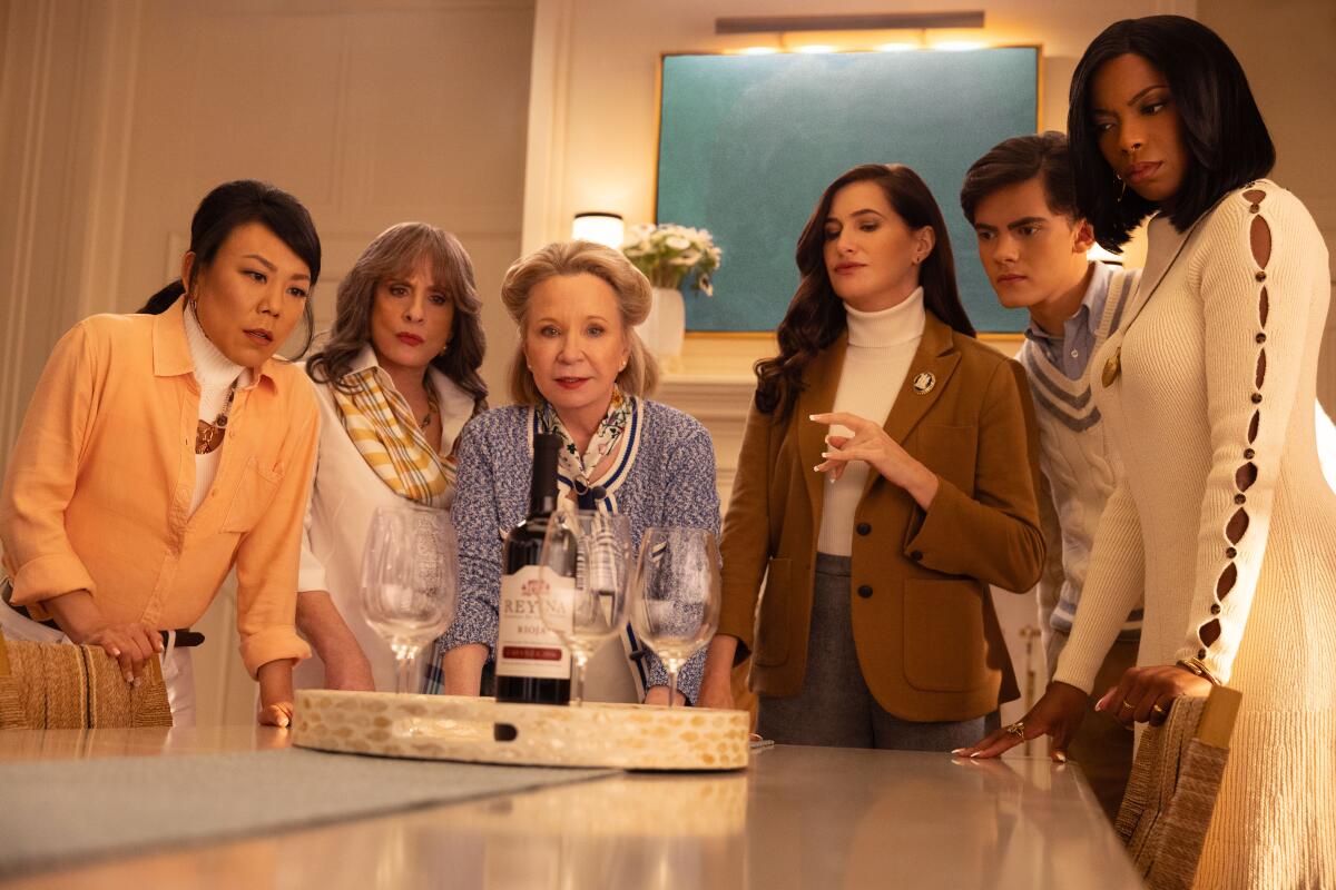 five women and a teenage boy looking at a bottle of win on a table