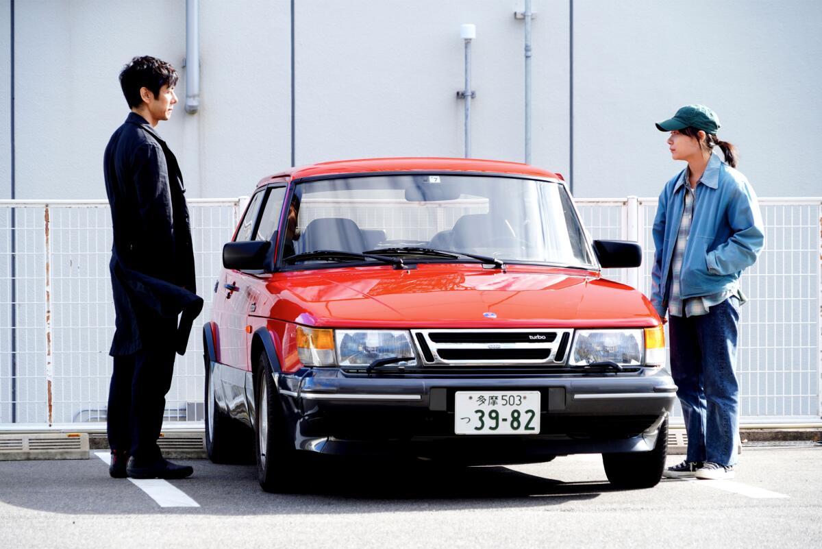 A man and woman stand next to a red car.