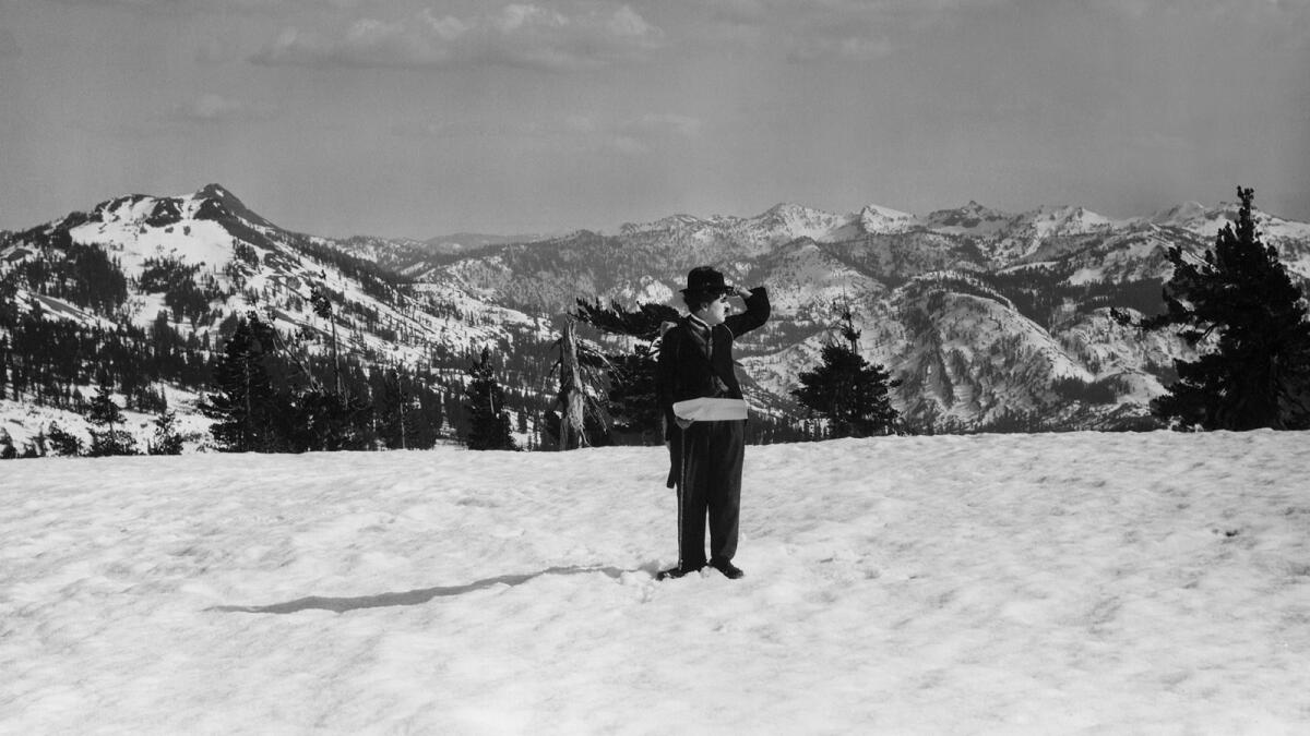 A man in a bowler hat stands on a snowy mountain.