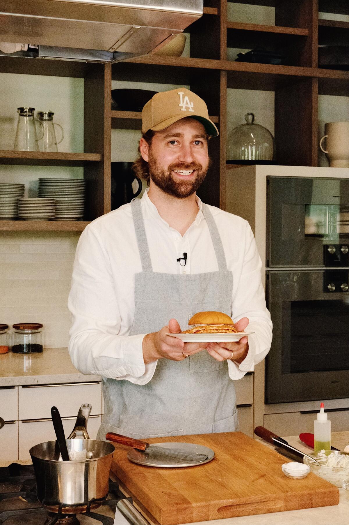 A vertical photo of chef Sean MacDonald holding his salmon smash burger on a plate in the L.A. Times Test Kitchen.