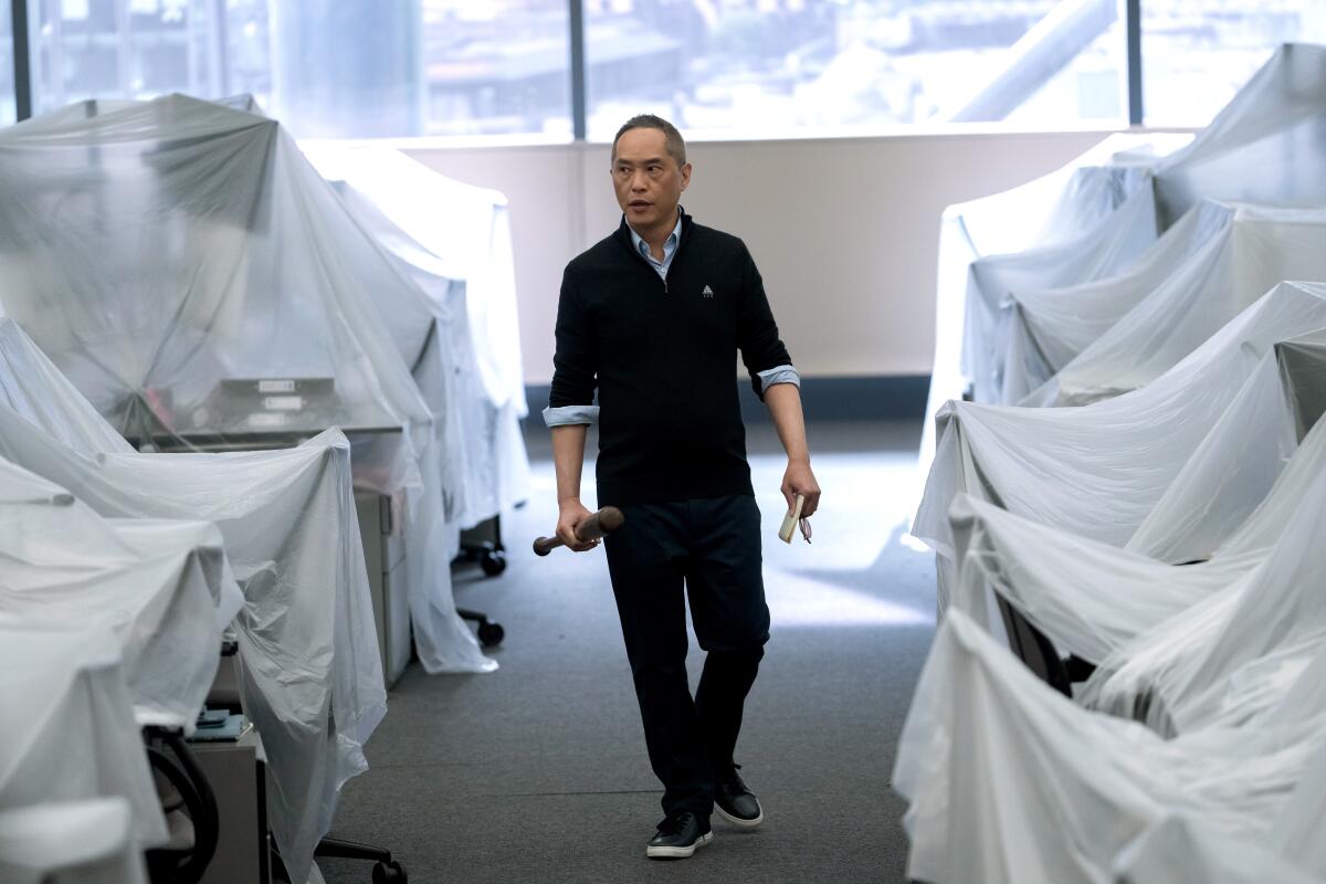 A man holding a baseball bat walks by desks covered in plastic