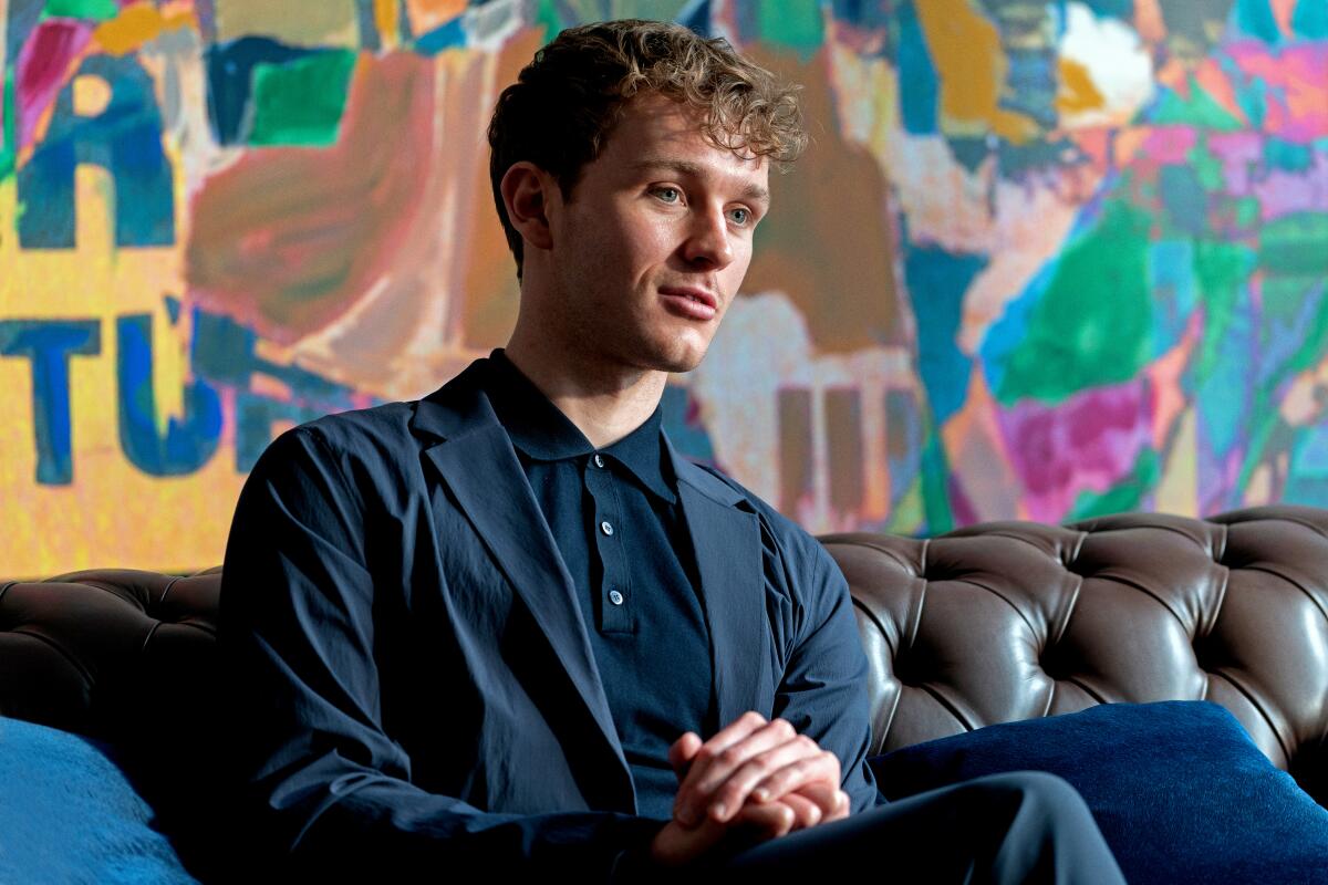 A man in a blazer sits on a couch