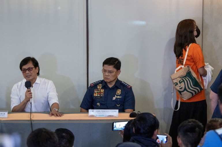 Alice Guo turning her back and looking at the wall. Philippines officials are sitting at a desk speaking to the media.