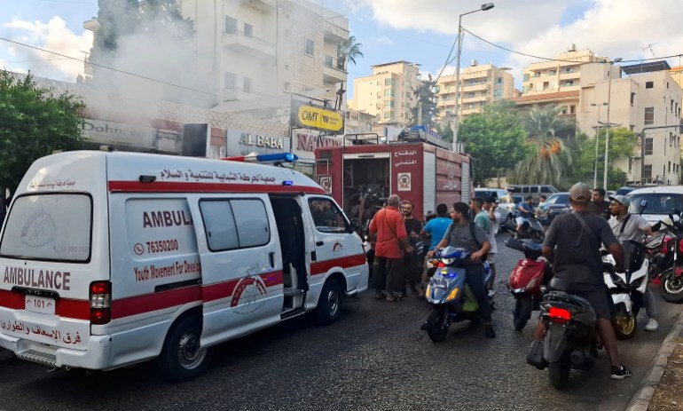 People gather as smoke rises from a mobile shop in Sidon