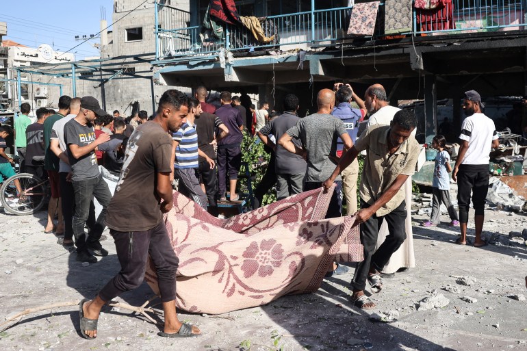 People use a blanket to transport a victim after an Israeli air strike hit a school in Nuseirat, in the central Gaza Strip