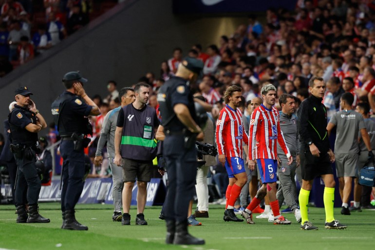 Atletico Madrid's French forward #07 Antoine Griezmann and Atletico Madrid's Argentine midfielder #05 Rodrigo De Paul leave the pitch after Atletico Madrid's supporters sent items on the pitch following Brazilian defender #03 Eder Militao's goal during the Spanish league football match between Club Atletico de Madrid and Real Madrid CF at the Metropolitano stadium in Madrid on September 29, 2024. (Photo by OSCAR DEL POZO / AFP)