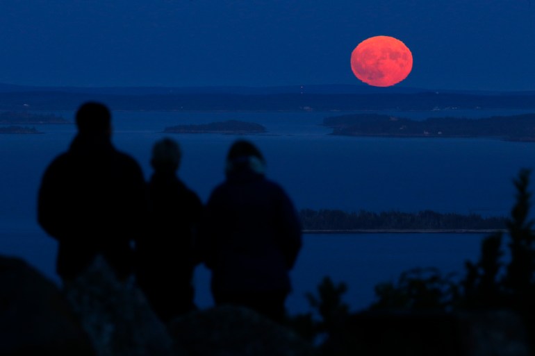 Three people watch the nearly-full harvest moon rise over Penobscot Bay