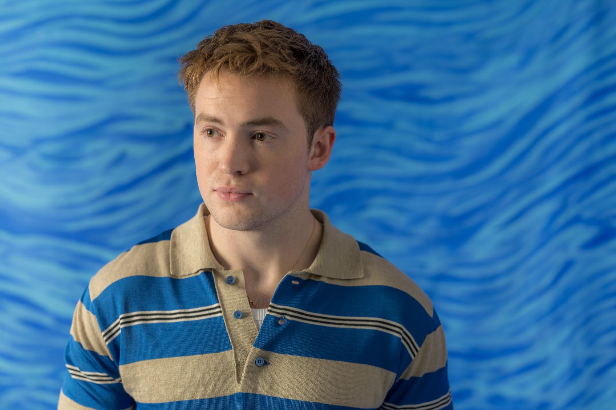 A man in a blue and tan striped shirt standing before a blue backdrop.