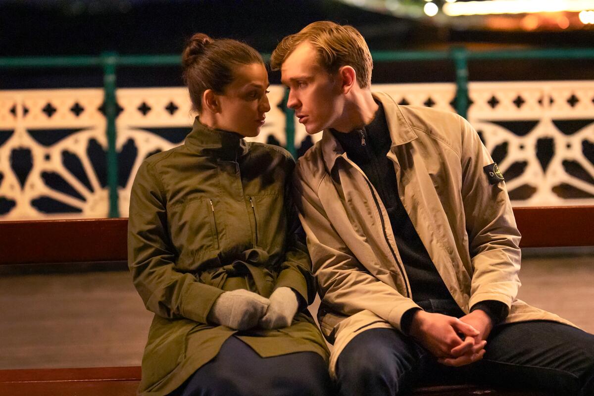 A woman and a man stare into each other's eyes about to kiss on a bench