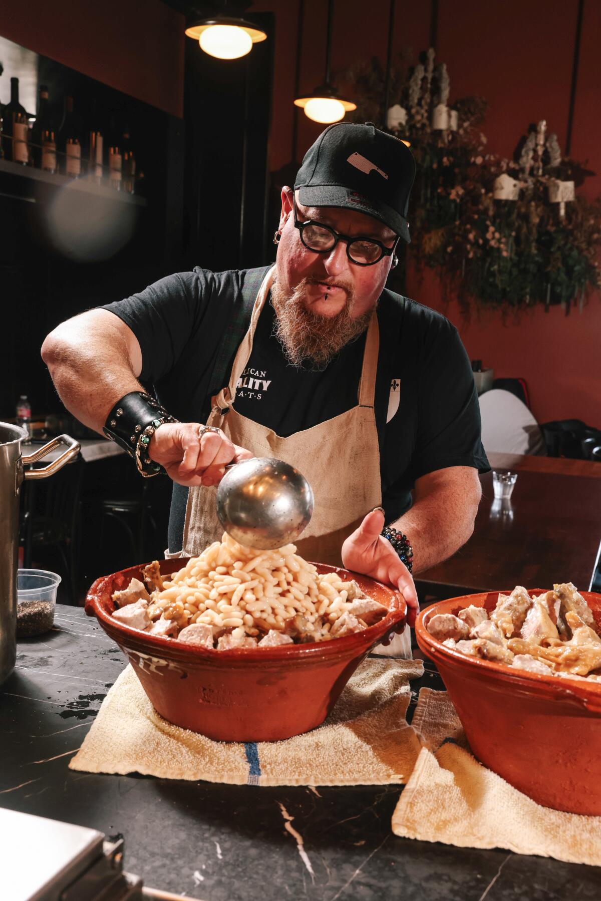 A bearded man in a black ballcap prepares food 