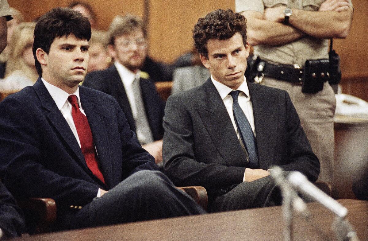 Two men in dark suits seated near a table in a courtroom.