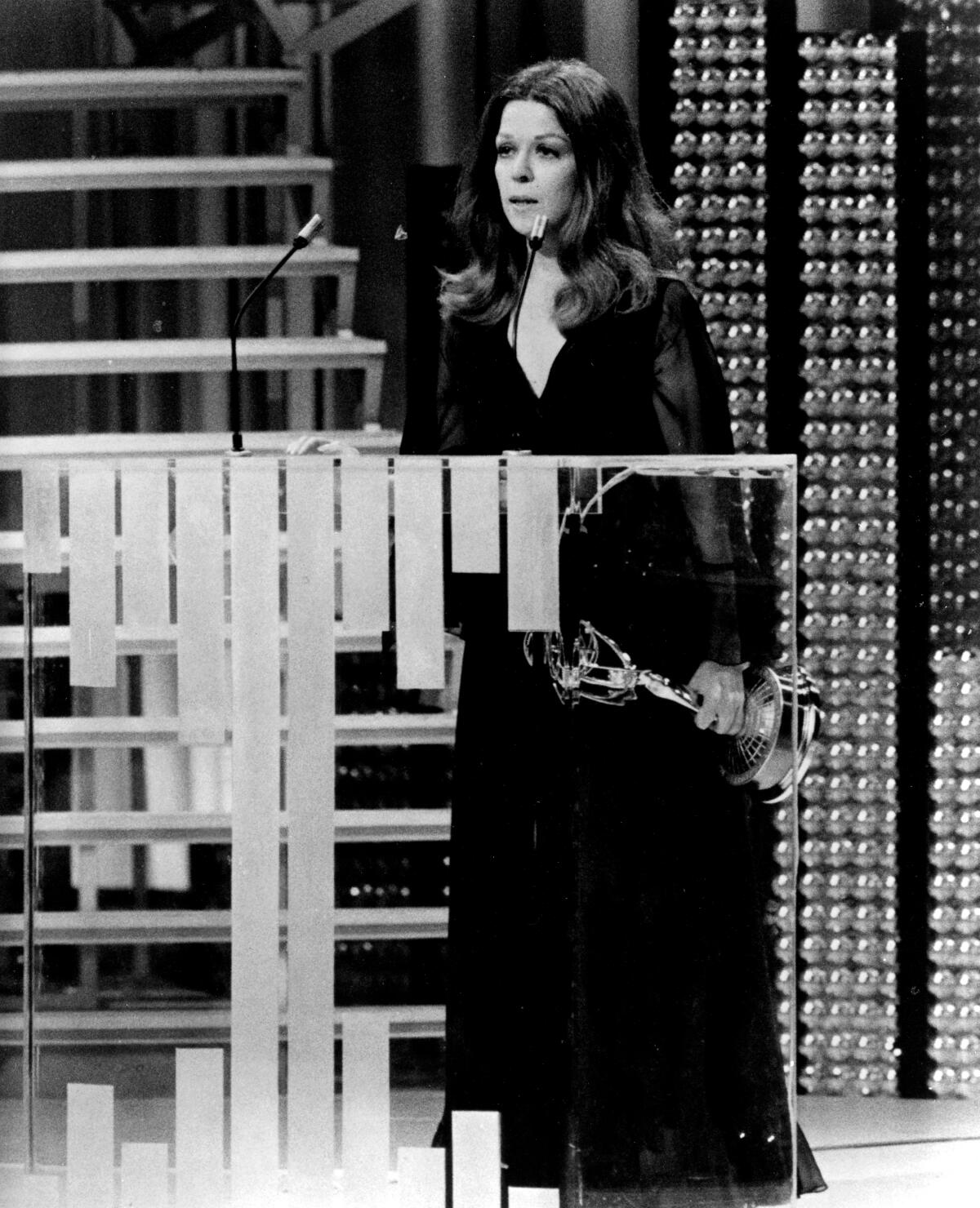 Treva Silverman stands behind a podium and holds an Emmy to her side.